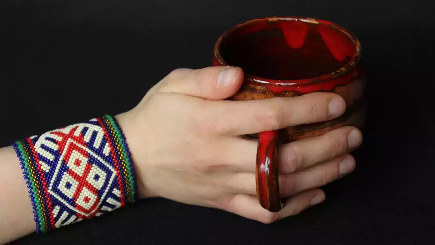 Ranka papuošta karoliukų apyranke laiko puodelį
