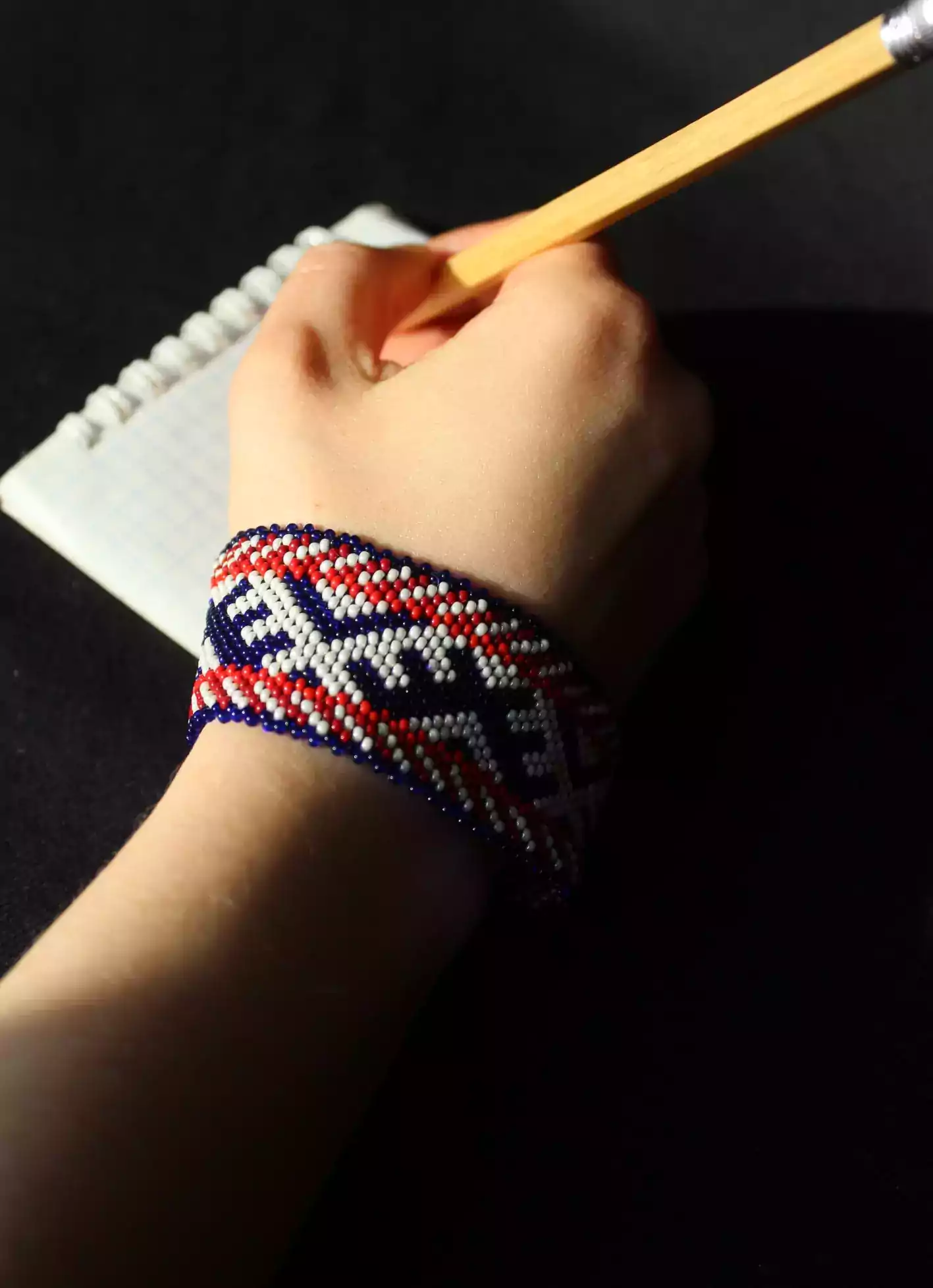 Ranka papuošta karoliukų apyranke rašo į užrašinę